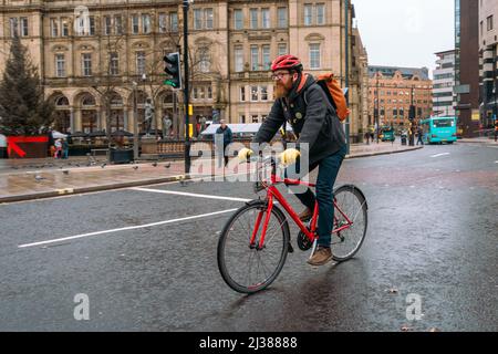 Pendlerradfahrer, die mit einem roten Helm und einem roten Fahrrad durch das Stadtzentrum von Leeds fahren. West Yorkshire, England, Großbritannien Stockfoto