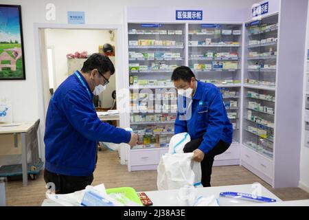 Shanghai, China. 5. April 2022. Der Deliveryman Ye Yifei (R) zieht Schutzkleidung an, bevor er sich in der Shanghai Pharma E Pharmacy in Shanghai, Ostchina, am 5. April 2022 aufmacht. Während der vorübergehenden geschlossenen Behandlungsdauer in Shanghai ist die Versorgung und Lieferung von Spezialmedikamenten an die Patienten, die diese benötigen, besonders wichtig. Eine Apotheke namens Shanghai Pharma E Pharmacy, die mehr als 260 neue Medikamente, Spezialmedikamente und Medikamente für seltene Krankheiten verkauft, bleibt im Geschäft, um die Medikamente zu liefern und zu liefern. Quelle: Jin Liwang/Xinhua/Alamy Live News Stockfoto