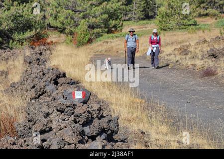 ÄTNA PARK, SIZILIEN - 22. OKTOBER 2017: Fokus auf Wanderzeichen, im Hintergrund verschwommenes Paar Wanderer mit Hund auf dem Weg zum Galvarina Plateau Stockfoto