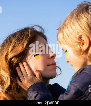 Das Gesicht des Teenagers wird von der Hand des kleinen Jungen, ihres Bruders, gehalten. Das Herz wird auf der Wange in den Farben der ukrainischen Flagge gezeichnet. Familie, Einheit, Trost. Nimm Stockfoto