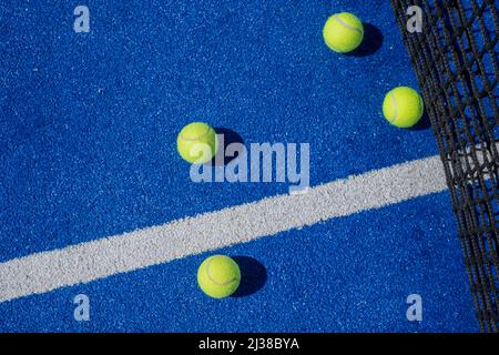 Selektive Fokussierung von vier Paddle-Tennisbällen auf einem blauen Paddle-Tennisplatz mit einem Netz im Hintergrund, Schlägersportkonzept Stockfoto