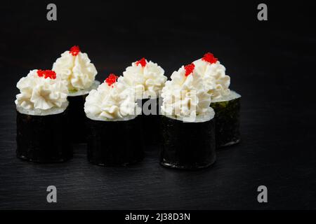 Sushi-Brötchen mit Meeresfrüchten, dekoriert mit Frischkäse und rotem Kaviar. Isoliert auf Schwarz, Nahaufnahme Stockfoto
