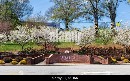 FORT MILL, S.C.-2. APRIL 22: 'Fort Mill'-Schild an der Ziegelmauer mit blühenden Hundewäldern am Eingang zur Main St. Bunte Kennung für die Stadt. Stockfoto