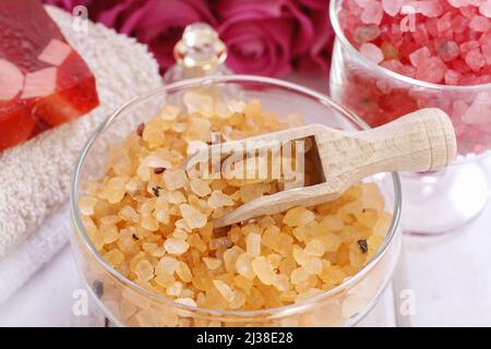 Glasschale mit gelbem Meersalz. Rosa Rosen im Hintergrund. Spa-Zeit Stockfoto