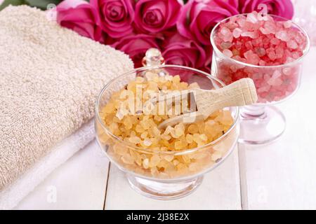 Glasschale mit gelbem Meersalz. Rosa Rosen im Hintergrund. Spa-Zeit Stockfoto