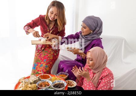 Porträts muslimischer Familie und Freunde feiern das Ende des Ramadan mit traditionellem Essen aus einem runden Tablett, das auf einem weißen Sofa auf weißem Hintergrund sitzt Stockfoto