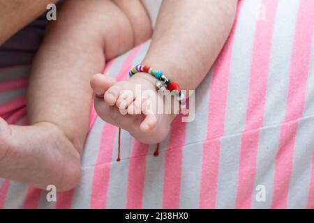 Nahaufnahme Detail der Füße eines Babys, das von ihrer Mutter getragen wird, während sie auf ihren Beinen schläft. Baby Füße mit Knöchelarmband, sehr bunt. Stockfoto