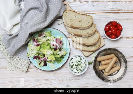 Frühstückstisch mit frischem Salat, Cottage, Brotscheiben und Würstchen. Gesunde Ernährung Stockfoto