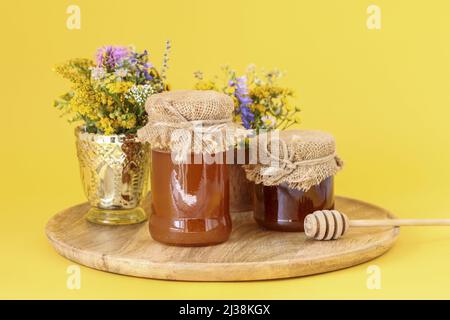 Gläser mit Honig und Blumensträußen auf gelbem Grund. Gesunde Ernährung Stockfoto