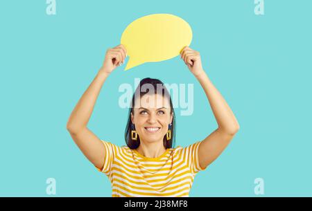 Glückliche junge Frau lächelt und hält einen leeren gelben Sprechballon oder eine Denkblase Stockfoto