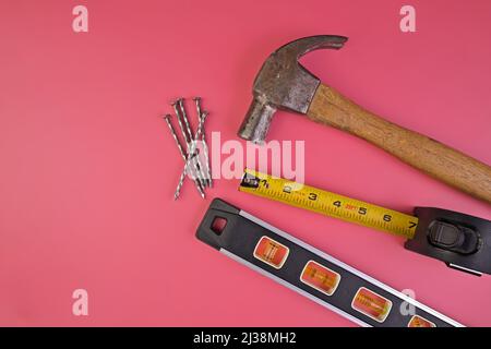 Flatlay von Hammer, Nägel, Maßband und Level isoliert auf einem rosa Hintergrund Stockfoto