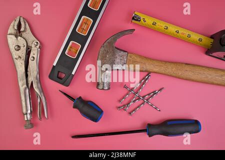 Flatlay von Handwerkzeugen auf rosa Hintergrund inklusive Hammer, Nägel, Maßband, Level, Schraubendreher Stockfoto