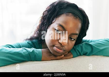 Traurige und schöne afroamerikanische Frau auf dem Sofa zu Hause Stockfoto