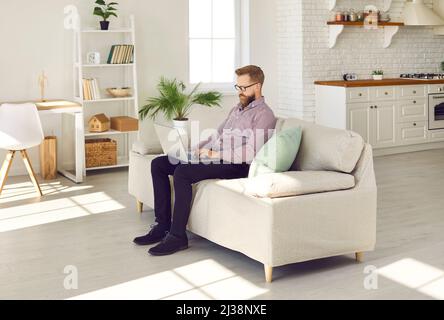 Mann mit Laptop arbeitet ferngesteuert, durchsucht soziale Netzwerke oder sucht im Internet nach Informationen. Stockfoto