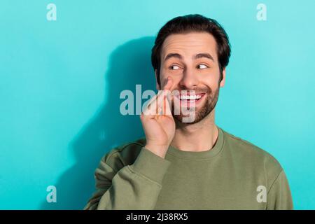 Foto von beeindruckt Bart Millennial Kerl sagen geheime tragen khaki Sweatshirt isoliert auf blauem Hintergrund Stockfoto