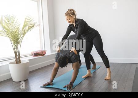 Persönlicher Trainer, der Yoga-Pose im sonnigen Studio mit dem Kunden macht Stockfoto