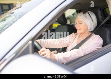 Fröhliche und lächelnde Seniorin im weißen Auto Stockfoto