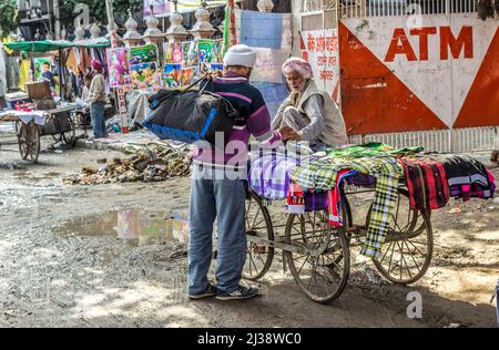 AMRITSAR, INDIEN - 24. FEBRUAR 2013: Der alte Händler verkauft in der Regenzeit in Amritsar, Indien, Kleidung an der überfluteten Straße. Stockfoto