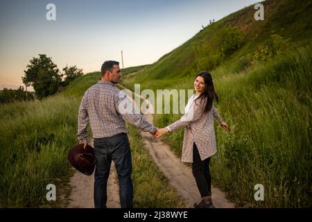 Schöner Mann und attraktive junge Frau, die an sonnigen Tagen auf einer verschneiten Landstraße spazieren gehen. Schöner Look, männliche und weibliche Mode, Winteroutfit. Winterurlaub, Wochenende auf dem Land Konzept. Stockfoto