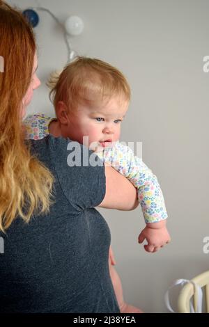 Nettes Mädchen, zehn Monate alt, das in den Armen ihrer Mutter spielt. Frohe Kindheit Stockfoto