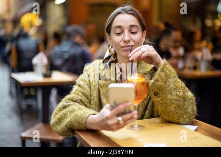 Frau mit Telefon und Getränk an der Bar im Freien Stockfoto