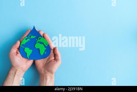 Papier Schnitt Wassertropfen mit Weltkarte innen auf blauem Hintergrund innerhalb der Handfläche. Speicherplatz kopieren. Tag der Erde. Stockfoto