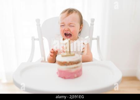 Der Kuchen zum ersten Geburtstag eines kleinen Mädchens sitzt weinend auf dem Stuhl Stockfoto