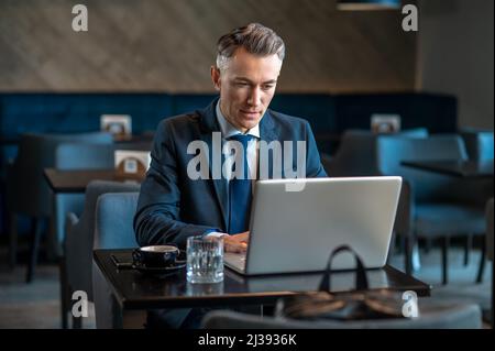 Ein Geschäftsmann mittleren Alters, der am Laptop sitzt und nachdenkt Stockfoto