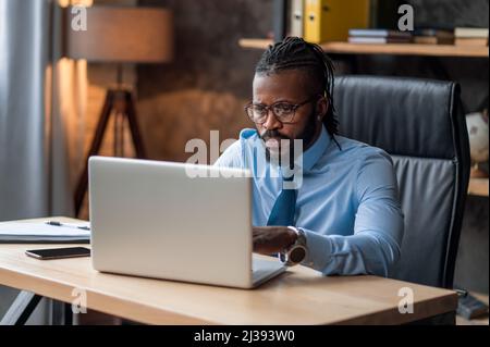 Konzentrierter Geschäftsmann in Brillen mit seinem Laptop Stockfoto