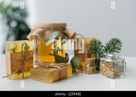 Handgemachte Seifenstücke neben Honig, Eukalyptus und Kräutern auf dem Tisch Stockfoto