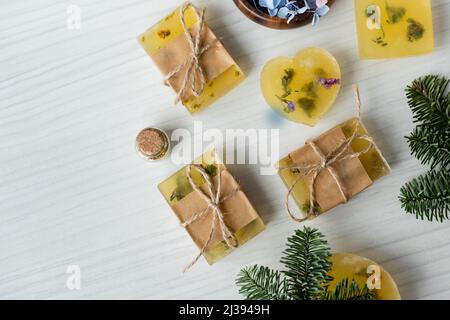 Draufsicht auf handgemachte Seifenstücke in der Nähe von Blumen und Kiefernästen auf dem Tisch Stockfoto