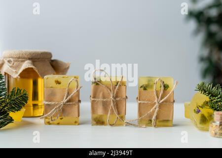 Handgemachte Seife mit Garn in der Nähe von Kiefernästen und verschwommener Honig auf dem Tisch Stockfoto