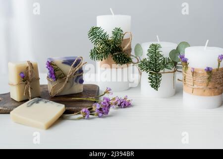 Handwerk Seifenstücke mit Blumen auf Schneidebrett in der Nähe von Kerzen auf dem Tisch auf grauem Hintergrund Stockfoto