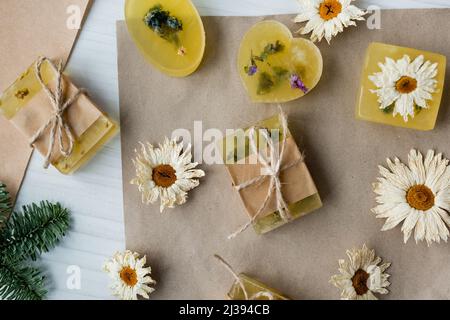 Draufsicht auf handgemachte Seife in der Nähe von trockenen Kamillen auf Bastelpapier auf dem Tisch Stockfoto