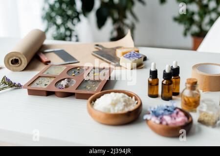 Handgemachte Seife in Silikonform in der Nähe von Essenzölen und verschwommenen Blumen auf dem Tisch Stockfoto