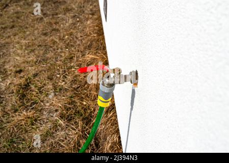 Der Hahn, der in offener Position aus der Fassadenwand herausragt und im Winter vor Frost geschützt ist. Stockfoto