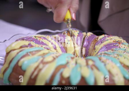 Nahaufnahme einer Frau, die in eine bunte Mardi Gras King Cake schneidet. Stockfoto
