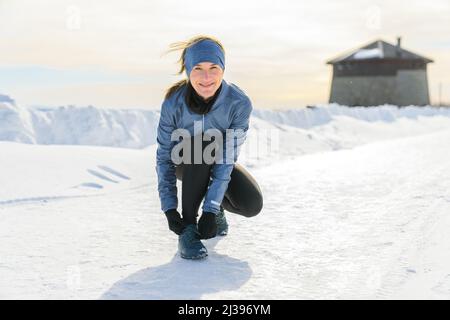 Frau, die in der Wintersaison im Snowy Park läuft, schnürt seine Schnürsenkel Stockfoto