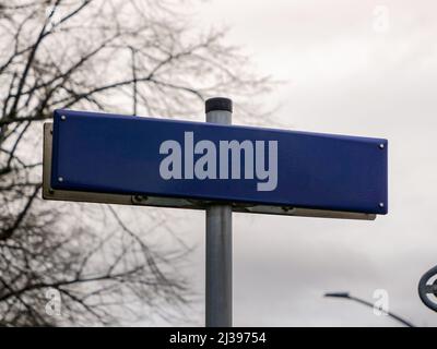 Leeres blaues Straßenschild in Deutschland. Leere Vorlage zum Einfügen eines Straßennamens. Metallplatte ohne Buchstaben für den Einsatz als Mockup. Führen Sie neben einem Weg. Stockfoto