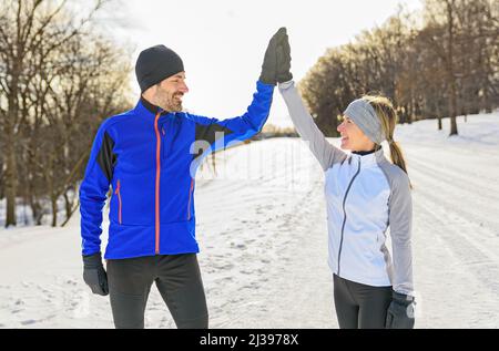 Reifes Paar im Winter läuft zusammen in der Natur geben eine hohe fünf mit ihrer Hand Stockfoto