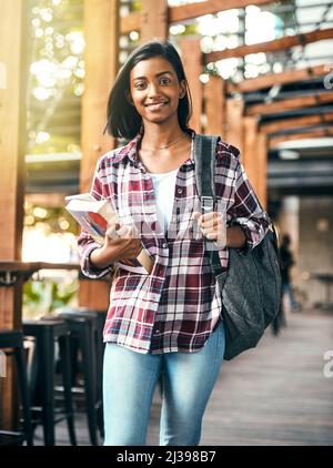 Das College-Leben passt zu ihr. Eine kleine Aufnahme einer jungen Studentin, die Lehrbücher auf dem Weg zur Klasse auf dem Campus hält. Stockfoto