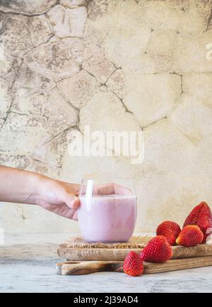 Hand von unkenntlichen Abholung ein Glas voll von leckeren hausgemachten Smoothie. Erdbeeren auf Holzbrett, hellgrüner Vintage-Hintergrund, Kopierplatz. Stockfoto