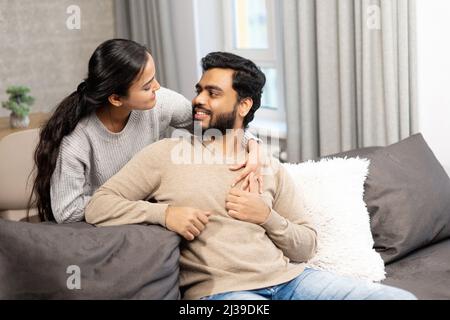 Sanftes und liebliches verliebter Paare, die auf dem bequemen Sofa zu Hause umarmt sitzen und sich zärtlich zuschauen. Konzept der Unterstützung und Fürsorge in der Ehe Stockfoto