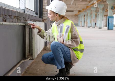 Eine Ingenieurin inspiziert alte Rohre und Heizkörper der Wasserheizung vor dem Wiederaufbau Stockfoto