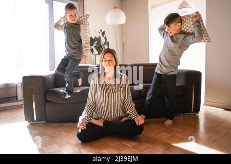 Unglückliche kaukasische Mutter leiden unter Kopfschmerzen, die müde vom Spielen eines frechen kleinen Sohnes gestresst werden. Stockfoto