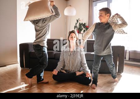 Unglückliche kaukasische Mutter leiden unter Kopfschmerzen, die müde vom Spielen eines frechen kleinen Sohnes gestresst werden. Stockfoto