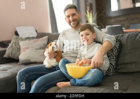 Vater oder Pate mit Basset Hund, der sich im Wohnzimmer zu Hause amüsieren kann, um sich einen Film mit Popcorn anzusehen Stockfoto