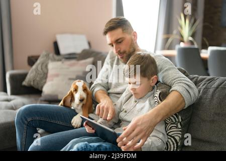 Vater oder Pate mit Basset Hund Spaß im Wohnzimmer zu Hause mit Computer-Tablet Stockfoto