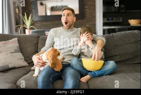 Vater oder Pate mit Basset Hund Spaß im Wohnzimmer zu Hause Film mit Popcorn sehen aus wie Angst Stockfoto