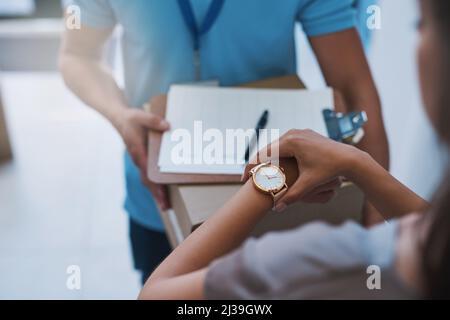 Ich habe dieses Paket erwartet. Ausgeschnittene Aufnahme einer nicht identifizierbaren Geschäftsfrau, die die Zeit auf ihrer Uhr überprüft, als der Kurier mit einer Lieferung eintrifft Stockfoto